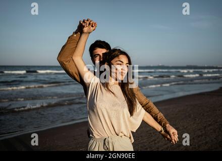 Jeune couple tenant les mains tout en dansant sur la plage Banque D'Images