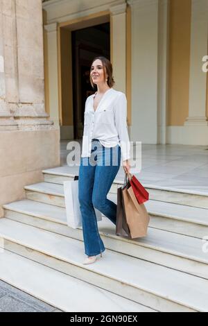 Femme souriante avec des sacs de shopping marchant sur l'escalier Banque D'Images