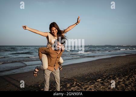 Femme joueur avec les bras débordés en appréciant le piggyback sur l'ami pendant le coucher du soleil Banque D'Images