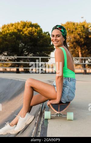 Femme adulte de taille moyenne assise sur un skateboard Banque D'Images
