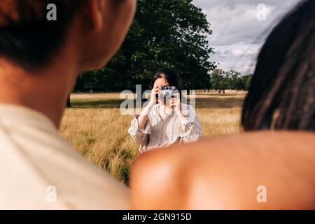 Femme photographiant des amis avec un appareil photo au parc Banque D'Images