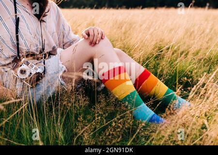 Femme avec caméra et chaussettes arc-en-ciel assis sur l'herbe Banque D'Images
