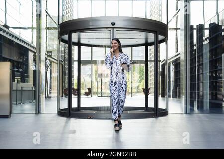 Jeune femme d'affaires avec ordinateur portable marchant devant la porte d'entrée Banque D'Images