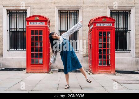 Femme aux bras dépassant l'équilibrage devant la cabine téléphonique Banque D'Images