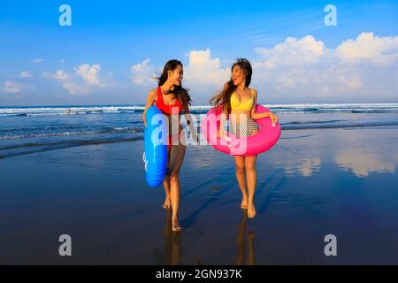 Des amies gaies avec des anneaux gonflables qui s'amusent à la plage Banque D'Images