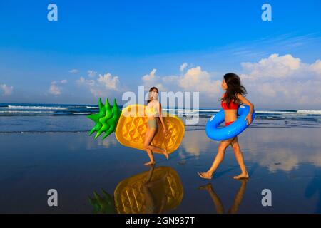 Des femmes souriantes tenant des flotteurs de natation marchant sur la plage Banque D'Images