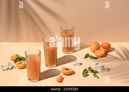 en été, il y a de nombreux verres de jus d'agrumes et de beaux abricots coupés. fond orange avec ombres de palmiers, espace de copie Banque D'Images