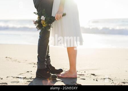 Mariée tenant le bouquet tout en se tenant debout avec marié à la plage Banque D'Images