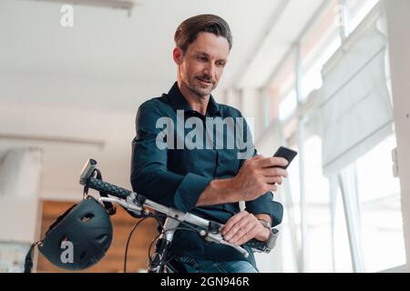 Homme d'affaires mature debout avec un vélo au bureau Banque D'Images