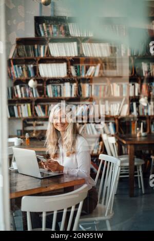 Femme mûre souriante aux cheveux gris au café Banque D'Images