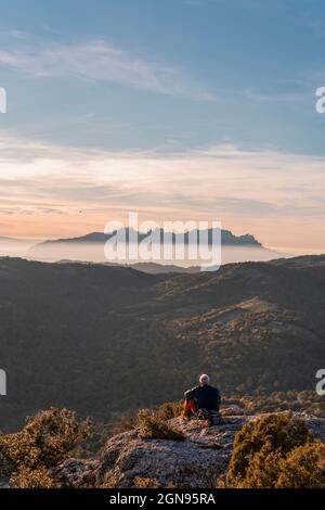 Homme senior regardant la montagne tout en s'asseyant sur la falaise pendant la randonnée Banque D'Images