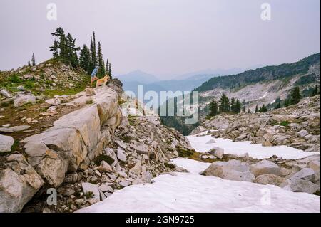 Randonneur mâle et chien moelleux debout sur une falaise dans les cascades du nord Banque D'Images