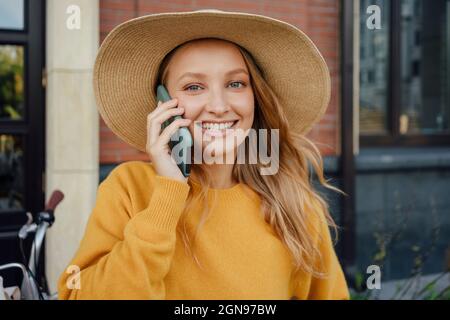 Belle femme blonde portant un chapeau parlant sur un smartphone Banque D'Images