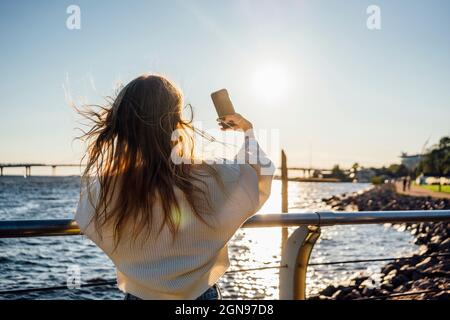 Une jeune femme prend le selfie à travers un smartphone par une main courante Banque D'Images