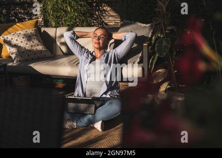 Femme fatiguée professionnelle se détendant avec les mains derrière la tête sur la terrasse Banque D'Images