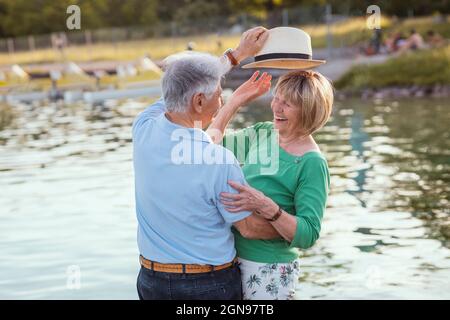 Homme âgé mettant le chapeau sur une femme joyeuse au bord du lac Banque D'Images