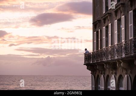 Un homme qui regarde la mer depuis son luxueux balcon au coucher du soleil Banque D'Images