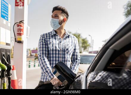 Homme avec masque facial de protection ravitailleur en gaz en voiture Banque D'Images