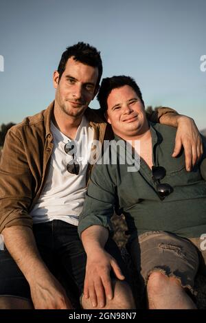 Homme assis avec le bras autour d'un ami au coucher du soleil Banque D'Images