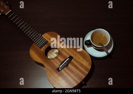 Ukulele en bois et une tasse de café au lait sur fond sombre Banque D'Images