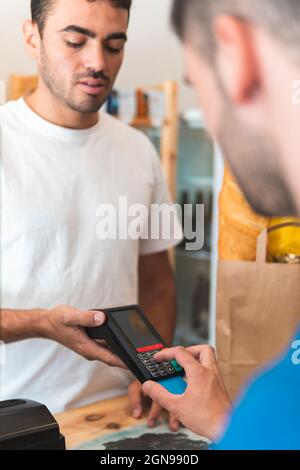 Client masculin payant par carte de crédit au propriétaire au magasin Banque D'Images