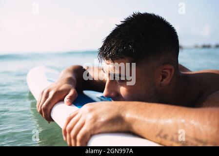 Jeune surfeur brunette reposant sur sa planche dans la mer. Banque D'Images