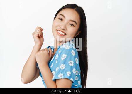 Portrait de belle fille asiatique souriant tendly, regardant l'appareil photo et la danse, ayant des dents blanches parfaites et une peau saine du visage sans maquillage Banque D'Images