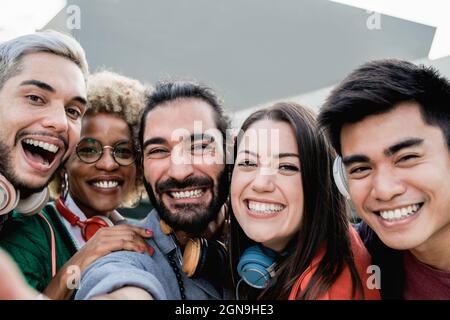 Amis multiraciaux s'amusant de prendre un portrait de selfie de groupe avec téléphone mobile en plein air dans la ville - Focus sur le visage de fille centrale Banque D'Images