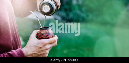 Homme préparant un compagnon avec de l'eau chaude. Gourd mate avec yerba à l'intérieur. Homme latino-américain d'âge moyen appréciant au coucher du soleil à l'extérieur. Format de bannière avec c Banque D'Images