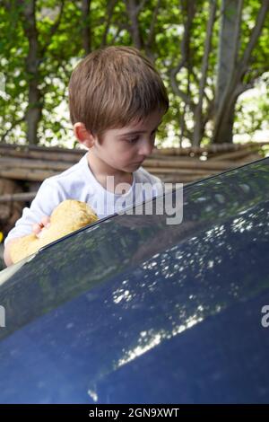 Voiture de nettoyage de garçon adorable petit garçon blond utilisant une éponge pour laver la voiture de ses parents pendant les vacances. Banque D'Images