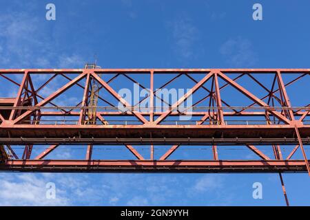 Structure industrielle suspendue peinte en rouge, isolée contre un ciel bleu vif, aspect horizontal Banque D'Images