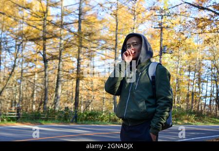 Jeune homme marchant dans la rue de la forêt d'automne à Kusatsu Onsen Town, Japon. Banque D'Images