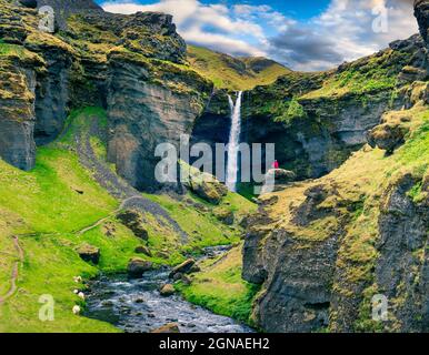 Vue colorée le matin sur la cascade de Kvernufoss. Scène majestueuse dans le sud de l'Islande avec homme méditant sur le bord de la falaise. Post-traitement de style artistique Banque D'Images