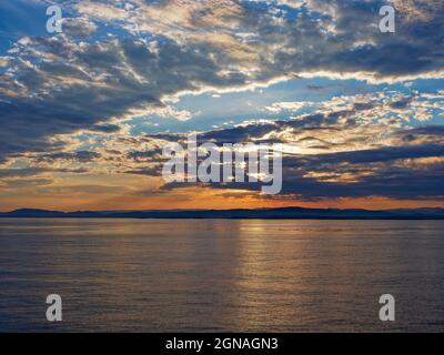 Surprenez la côte sauvage de la Norvège occidentale avec les nuages bas taillés orange et jaune par le soleil levant, le matin d'un été calme. Banque D'Images