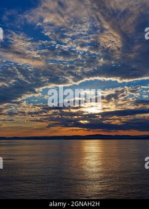 Lever du soleil sur la côte ouest norvégienne sauvage avec les nuages bas taillés orange et jaune par le soleil levant, le matin d'un été calme. Banque D'Images