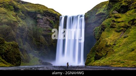 Homme voyageur qui vit la cascade à couper le souffle de Skogafoss en Islande. A l'échelle de la cascade par rapport à la taille de l'homme Banque D'Images