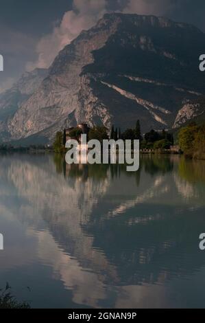 Les rochers de dolomite surplombent Castel Toblino, un château médiéval sur le Lago di Toblino dans le Trentin-Haut-Adige, Italie. Par une journée tranquille de septembre, le soleil tôt le matin crée des reflets bleu-vert chatoyants sur la surface du lac. Le château, fondé dans les années 1100, était autrefois une formidable forteresse et plus tard une retraite d'été pour les princes-évêques de trente. Il dispose maintenant d'un élégant restaurant au bord de l'eau avec terrasse ensoleillée. Banque D'Images