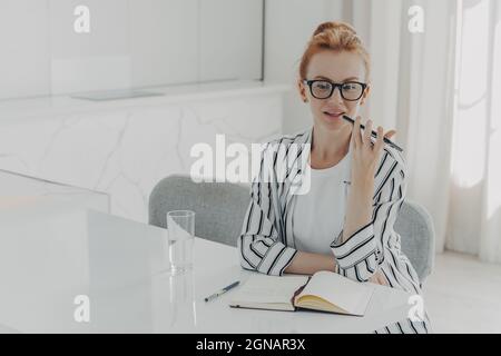 Photo d'une jeune femme à tête rouge qui enregistre les appels vocaux via le microphone du smartphone placé sur le bureau Banque D'Images