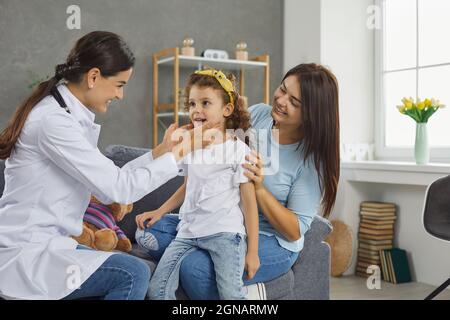 Une femme sympathique médecin lors d'une réunion avec la famille examine une petite fille mignonne pour le mal de gorge. Banque D'Images