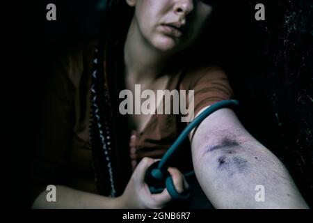 La femme drogué tire sa main avec le tourniquet. Ponction des plaies et des ecchymoses sur le bras de la femme. Fille adulte avec des dreadlocks avant de prendre la dose de stupéfiant dans la veine. Banque D'Images