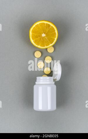 Vitamine C dans un pot blanc avec des citrons. Pilules jaunes, fruits et suppléments à base de plantes. Photo verticale. Vue de dessus. Banque D'Images