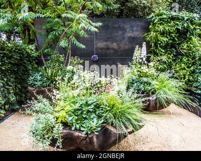 Une terrasse en gravier avec chaise et récipients richement plantés. Banque D'Images