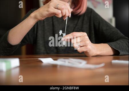 Vue avant d'une femme effectuant un test rapide de 19 Covid à la maison - en trempant un coton-tige dans une solution. Banque D'Images