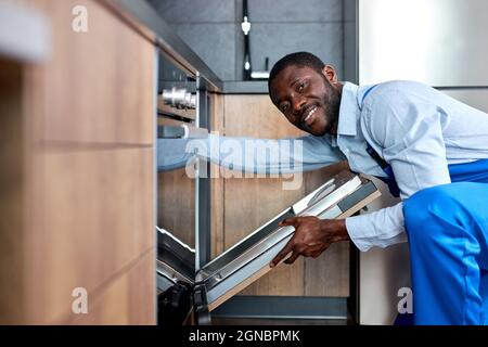 Happy Smiling Professionnel Africain American Handy in Blue overalls Uniform va réparer lave-vaisselle, confiant entrepreneur l'examiner avant Banque D'Images