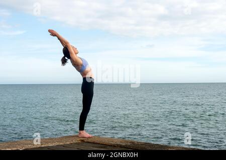 Poses de yoga. Femme debout dans le backbend Asana pratiquant à Anuvittasana pose au bord de la mer. Banque D'Images