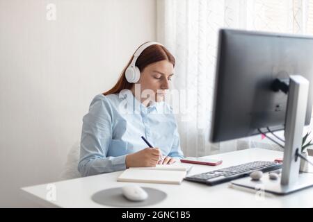 Apprentissage à distance, éducation et travail. Femme tenant le stylo à la main sur le bloc-notes à la maison, écrit des objectifs, des plans, faire à faire et liste de souhaits sur le bureau, à partir de Banque D'Images