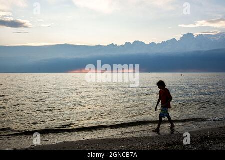 Un garçon en silhouette marche le long de la plage avec des nuages de tempête s'édifier à l'horizon lointain. Copier l'espace. Banque D'Images