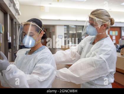SAN DIEGO (août 4, 2020) Ensign Kaitlyn Leibing, à droite, une infirmière affectée à l'un des services de médecine interne du Centre médical naval de San Diego (NMCSD), aide l'Hospitalman Angela Mello, un corpsman de service général affecté au NMCSD, à ne pas utiliser d'équipement de protection individuelle (EPI), Y compris un écran facial imprimé en 3D donné à l’hôpital par Naval information Warfare Systems Command, avant d’entrer dans une chambre de patient non critique positive COVID-19, 4 août 2020. Les écrans faciaux, les masques respiratoires N95, les gants et les blouses sont quelques-uns des EPI nécessaires pour entrer dans les espaces COVID-19-patient. La mission du NMCSD est de préparer Banque D'Images