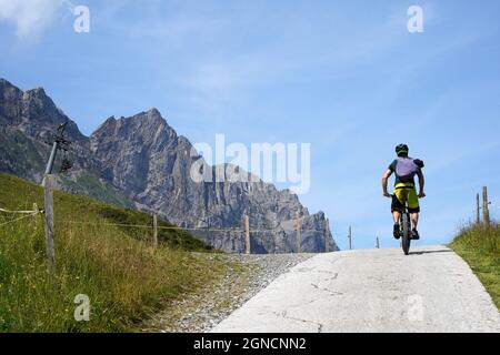 Homme sur un vélo sur une colline, vue arrière.Il y a les montagnes Alp sur la gauche.Piste cyclable et de randonnée dans la région d'Engelberg en Suisse Banque D'Images