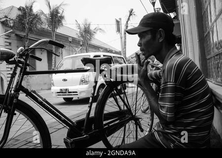 Photo en noir et blanc d'un chauffeur de taxi à vélo prenant une pause. Dans la région de Kota Lama, Jakarta, il y a plusieurs cyclistes qui peuvent prendre des touristes. Banque D'Images